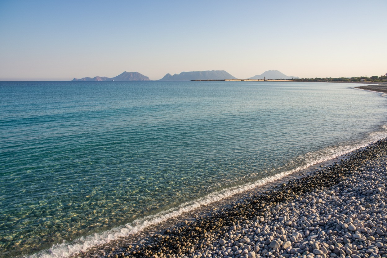 Spiaggia di ciottoli bagnata da un mare limpido con le isole Eolie visibili all'orizzonte.